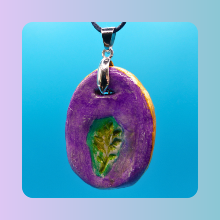Vue de face du pendentif Petit Lien en argile autodurcissante, pièce unique, fait main, de couleur violette, forme organique allongée, surface douce et brillante. Posé sur fond bleu.