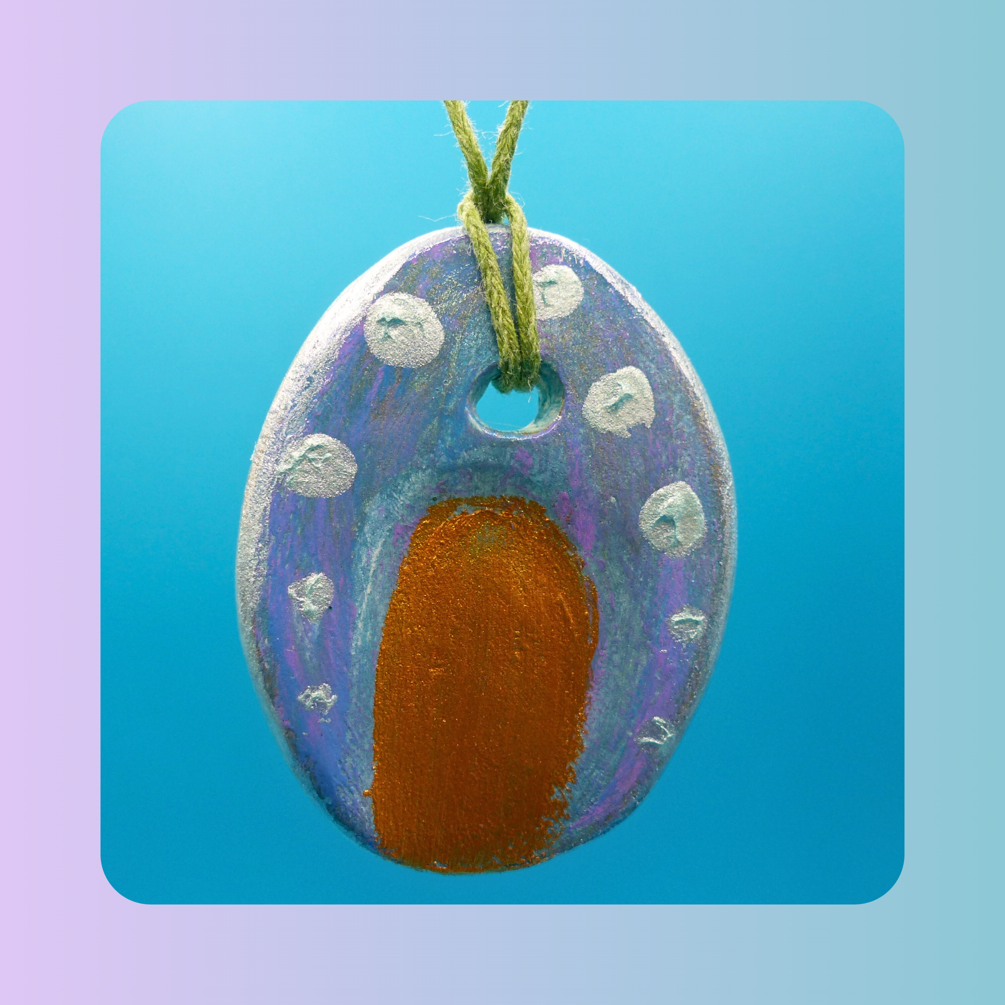 Vue de face du pendentif Petit Lien en argile autodurcissante, pièce unique, fait main, couleur bleu et doré, forme organique allongée, surface douce et brillante. Posé sur fond bleu.