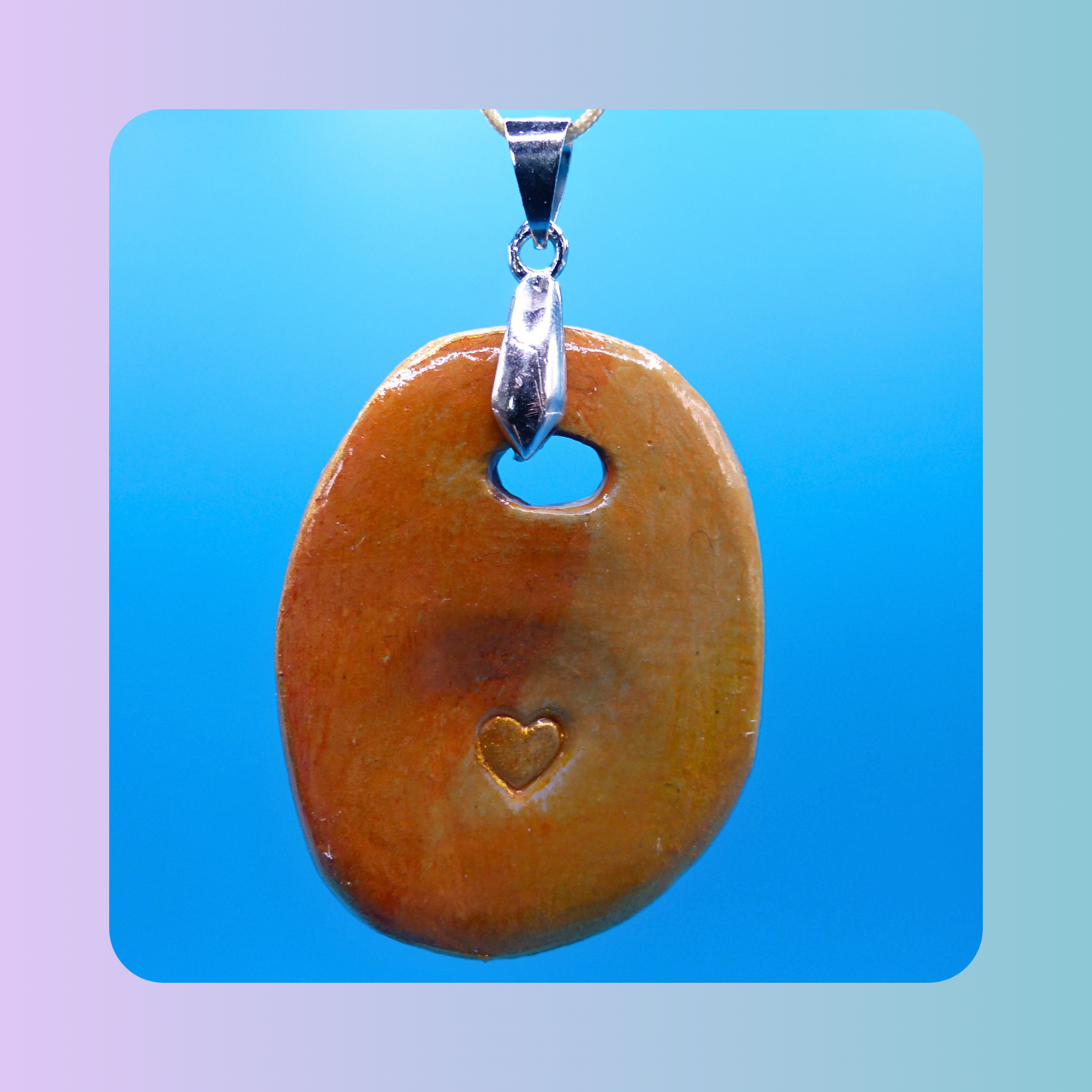 Vue de face du pendentif Petit Lien en argile autodurcissante, pièce unique, fait main, couleur orangée, forme organique allongée, surface douce et brillante. Posé sur fond bleu.