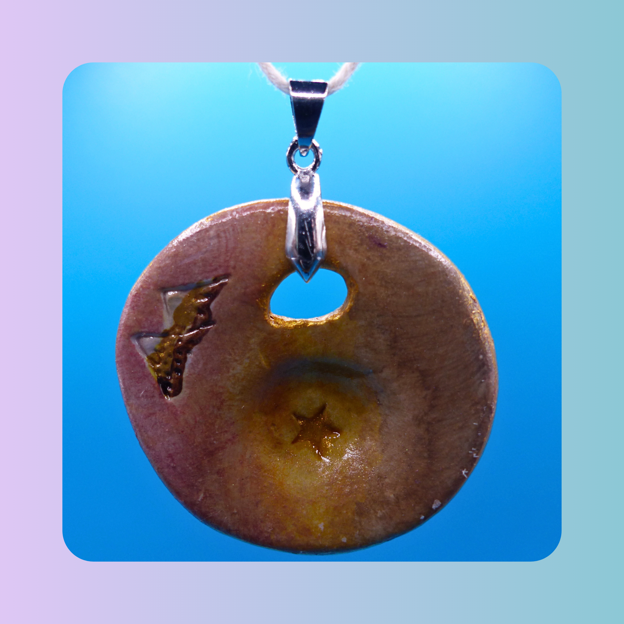 Vue de face du pendentif Petit Lien en argile autodurcissante, pièce unique, fait main, couleur sable, forme organique ronde, surface douce et brillante. Motif montagne et étoile. Posé sur fond bleu.